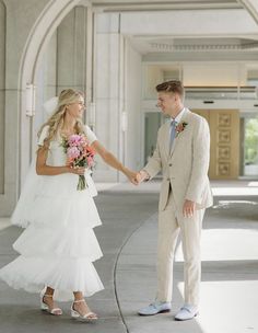 a bride and groom holding hands in front of an arch at the entrance to a building