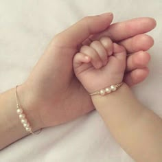 two hands holding each other on top of a white bed with a baby's hand in the middle