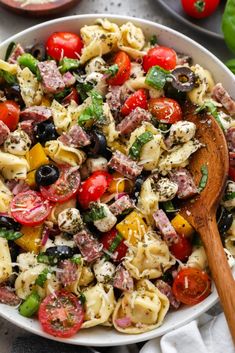 a pasta salad with tomatoes, olives, and other ingredients in a white bowl