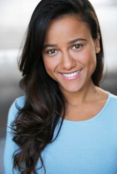 a woman with long dark hair smiling at the camera and wearing a blue sweater on