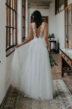 a woman in a white wedding dress is standing on a rug and looking out the window