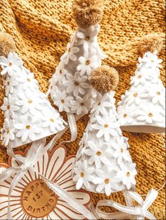 three white knitted christmas trees with pom - poms and ribbons on a yellow blanket