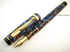 two fountain pens sitting next to each other on top of a white surface with gold trimming