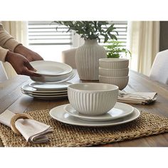 a person setting a table with white dishes and placemats on top of it