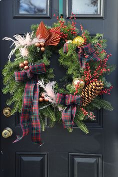 a christmas wreath on the front door with pine cones, holly and other holiday decorations