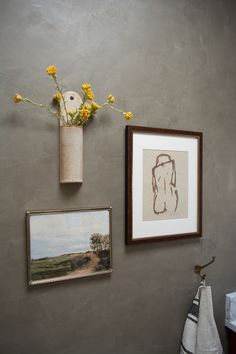 two framed pictures hang on the wall next to a vase with yellow flowers in it