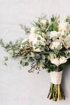 a bridal bouquet with white flowers and greenery on the stems is displayed against a white background