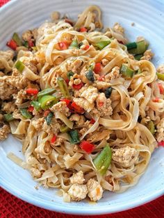 a white bowl filled with noodles and meat on top of a red table cloth next to a fork