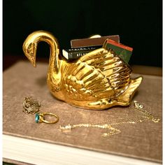 a gold swan figurine sitting on top of a book next to some jewelry