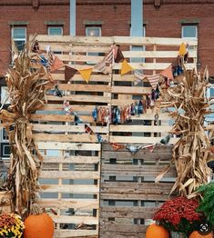 pumpkins and corn stalks are displayed in front of a wooden fence with bunting