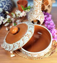 two vases with flowers in the background and one has a lid on it that is sitting on a table