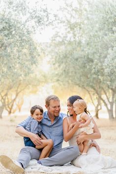 a man, woman and two children sitting on a blanket in the middle of an olive grove