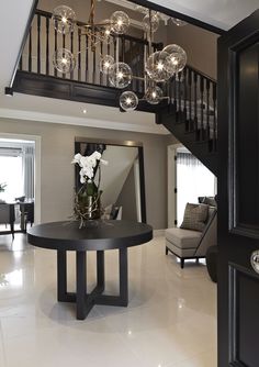 a living room filled with furniture and a chandelier hanging from the top of a stair case