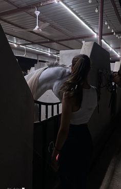 a woman standing next to a white horse in an indoor area with lights on the ceiling