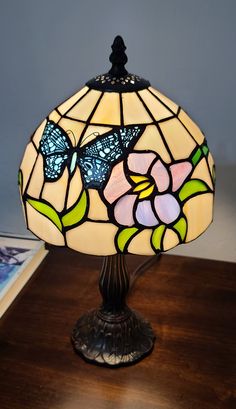 a stained glass lamp on a wooden table with a butterfly and flower design in the shade