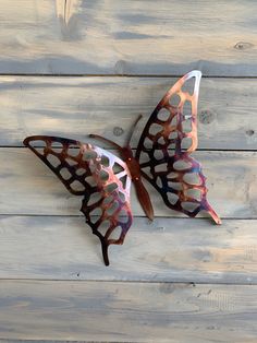 a metal butterfly sitting on top of a wooden floor next to a wall with holes in it's wings