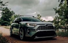 the front end of a gray toyota rav parked on a dirt road next to trees