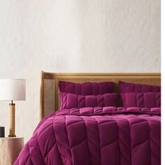 a bed with a purple comforter and pillows on it, next to a lamp