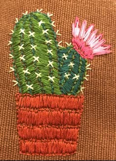 an embroidered cactus with pink flowers in a pot on a brown cloth background, close up