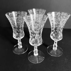 four glass goblets sitting on top of a black table next to each other