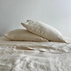 two pillows on top of a bed with white sheets and linens in the background