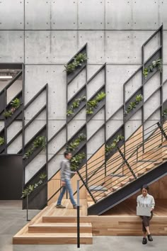 two people are walking up and down the stairs in an office building with plants growing on them