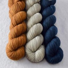 four skeins of yarn are lined up on a white surface, one is blue and the other is orange