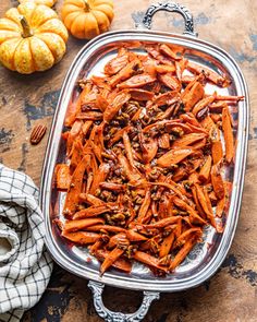 cooked carrots in a serving dish on a table next to small pumpkins and a towel