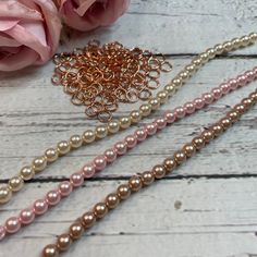 three different colored pearls on a white wooden table next to pink roses and a rose bud