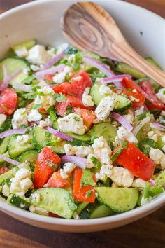 a white bowl filled with cucumber, tomatoes and feta cheese next to a wooden spoon