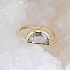 a gold ring with a white diamond on top of some ice crystals and rocks in the background