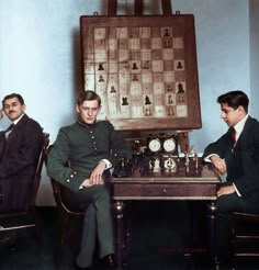 three men sitting at a table playing chess