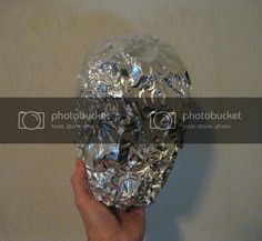 a hand holding up a foil covered object in front of a white wall and floor