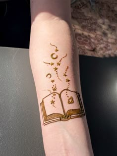 a person with a tattoo on their arm holding an open book and stars in the sky