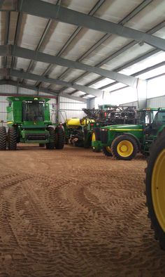 several tractors are parked in a building with metal roofing and yellow tires on the ground