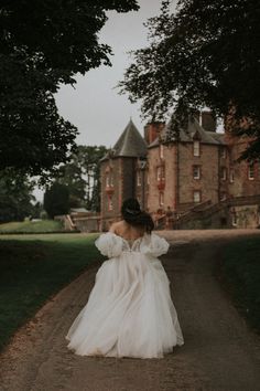 a woman in a white dress walking down a dirt road