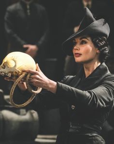 a woman is holding a human skull in her right hand and wearing a black hat