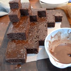 there are brownies on the cutting board and a bowl of chocolate sauce next to it