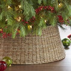 a christmas tree in a wicker basket with red berries and pine cones around it