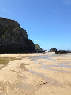 a sandy beach next to the ocean under a blue sky with some rocks on it