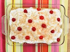 a cake with coconut and cherries in a glass dish on a colorful table cloth