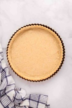 an uncooked pie crust in a pan on a marble counter top with a blue and white checkered napkin