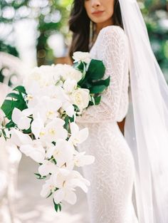 a woman in a wedding dress holding a bouquet of flowers and wearing a long veil