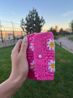 a hand holding up a pink crocheted cloth with flowers on it in the grass