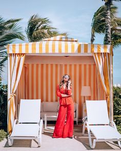 a woman standing in front of a yellow and white striped gazebo with two lounge chairs