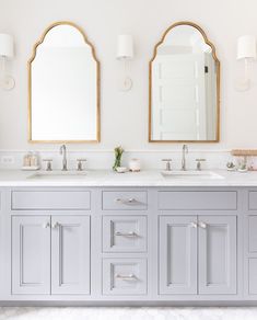 two mirrors are above the double sinks in this white and gray bathroom with gold trim