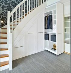 a white closet under a stair case in a room with blue wallpaper and wooden flooring