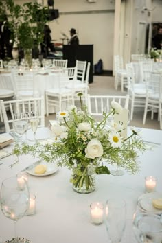 a vase filled with white flowers sitting on top of a table covered in plates and glasses