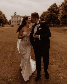 a bride and groom kissing in the middle of a field with an old house in the background