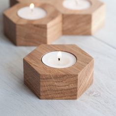 three wooden hexagonal candle holders with lit candles in them on a white surface